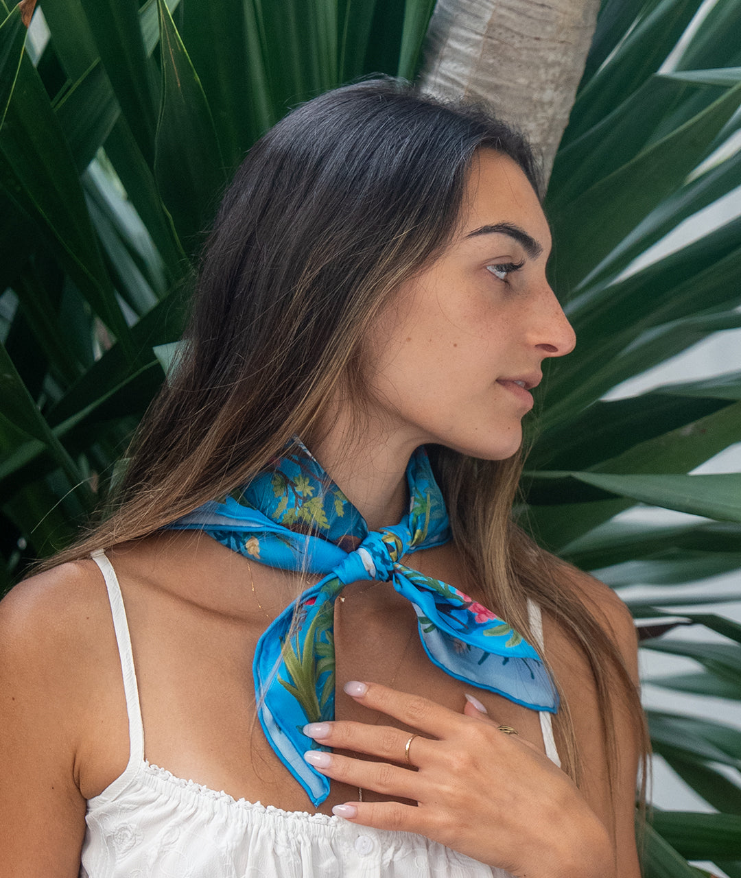 Woman wearing a blue botani bloom silk scarf against a tropical background