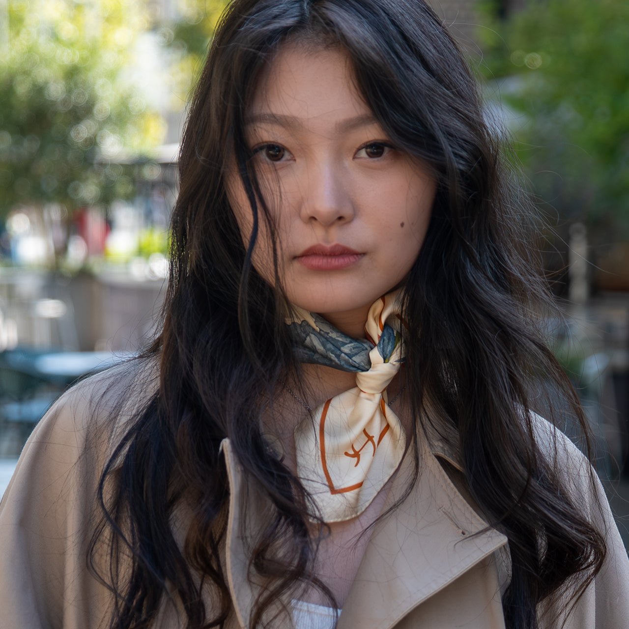 Woman wearing a beige coat and scarf with a blurred outdoor background