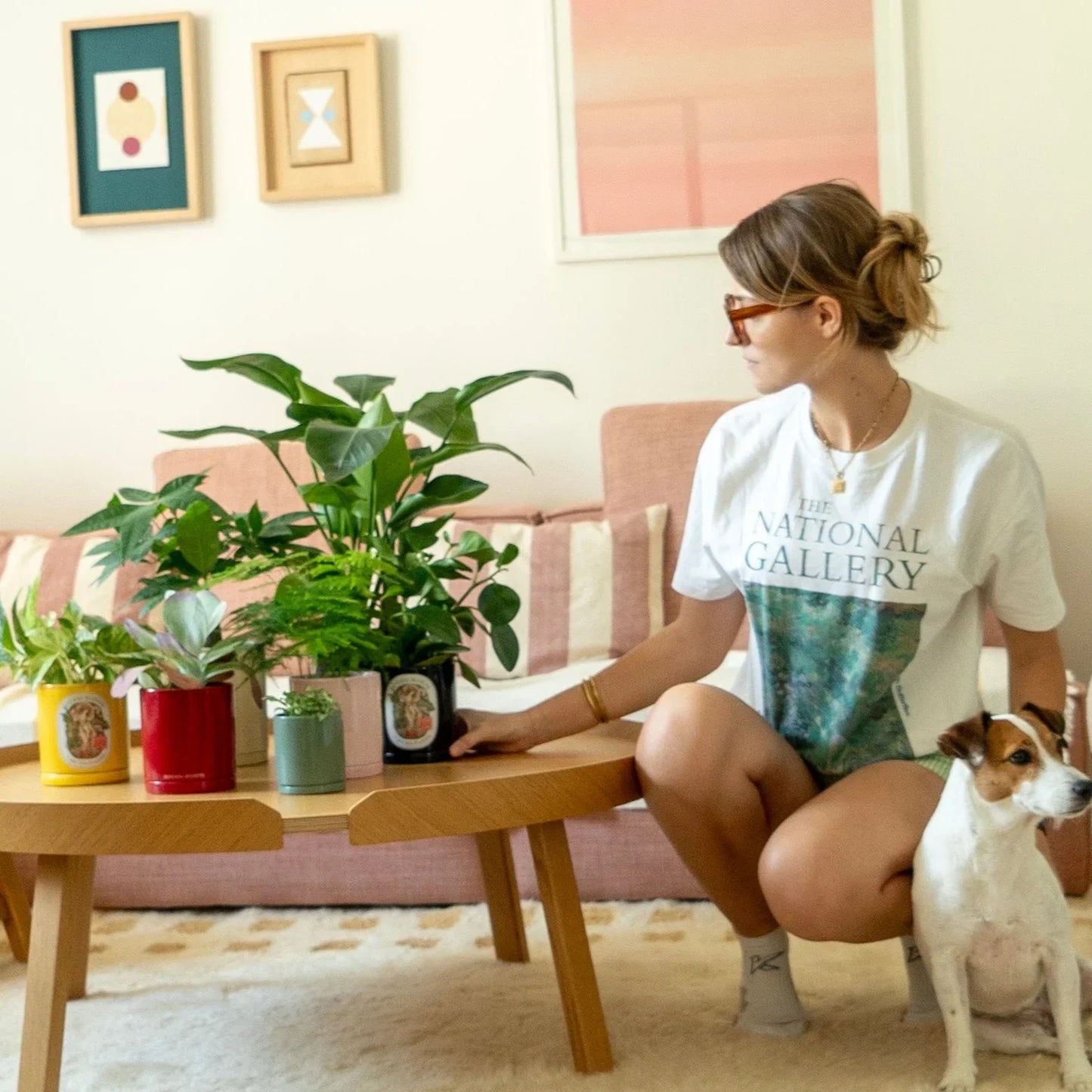 Woman sitting on a couch with a dog, surrounded by botani bloom potted plants in a living room.