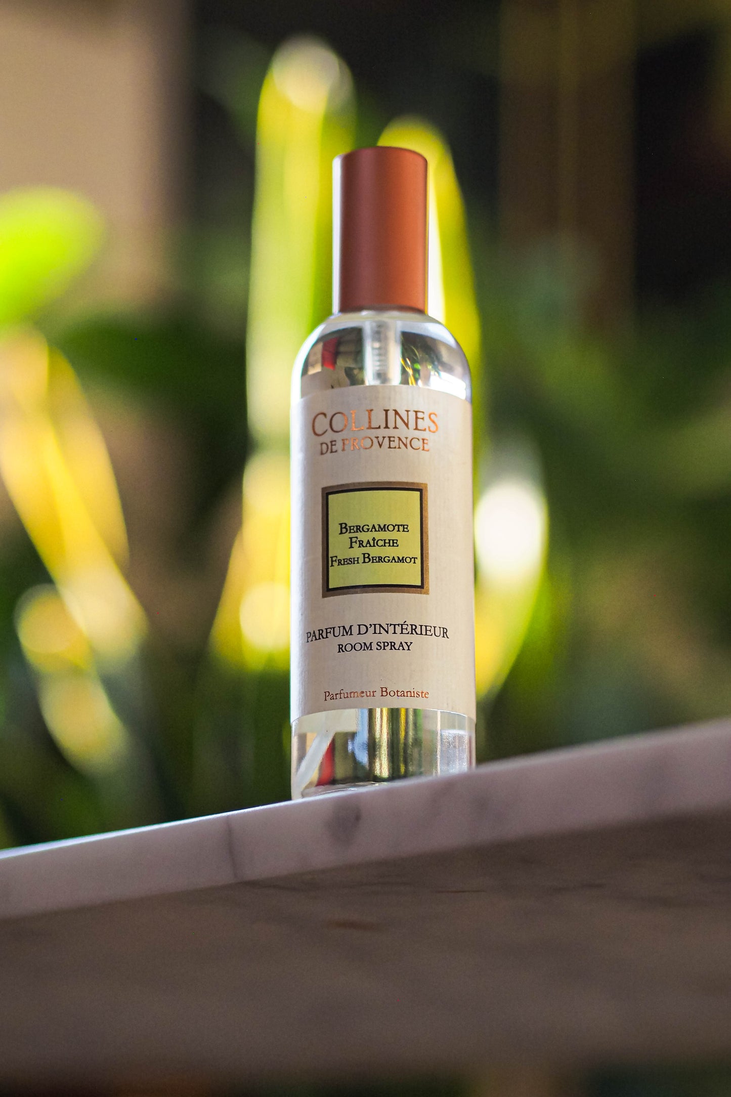 A bottle of Fresh Bergamote Room Spray, placed on a marble surface with greenery in the background.