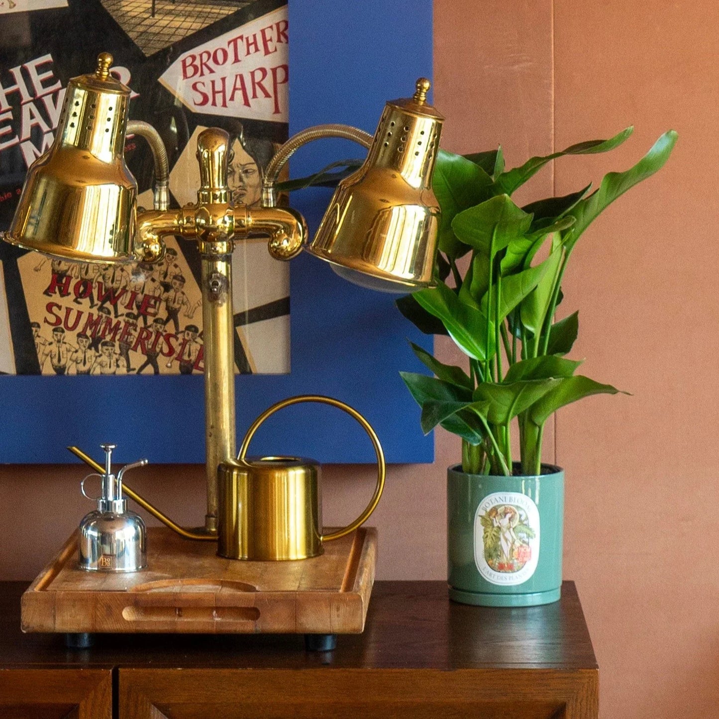 A potted bird of paradise, housed in an olive botani bloom pot, with botani bloom plant mister and watering can