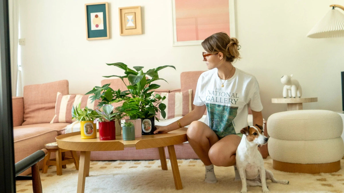 A woman in a cozy indoor setting interacts with house plants and scented candles from Botani Bloom, showcasing the benefits of plant care and enhancing well-being.
