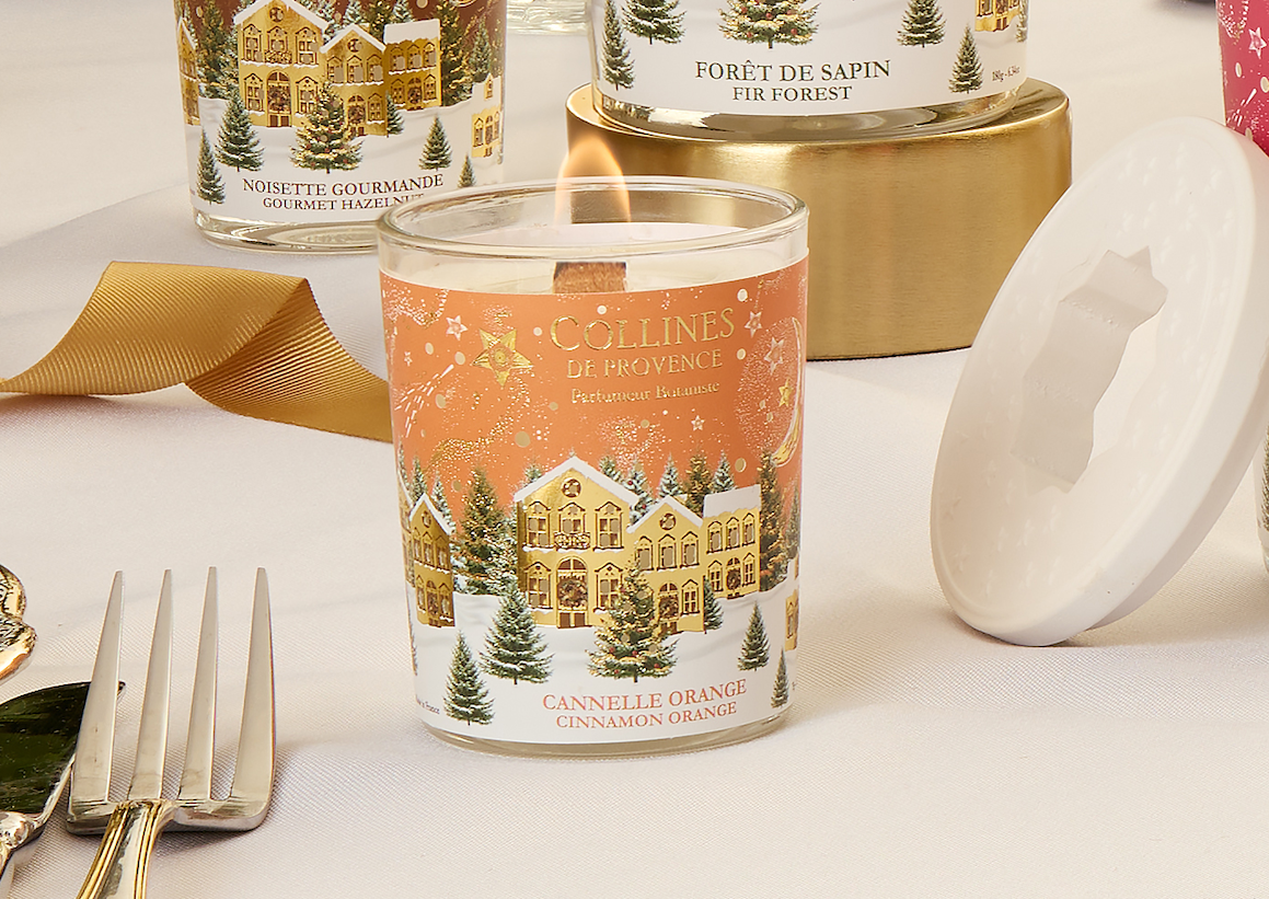 Collines de Provence 75g cinnamon orange scented candle with Christmas-themed design on a table with gold ribbon and silverware.