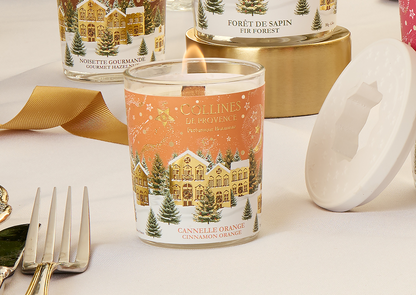 Collines de Provence 75g cinnamon orange scented candle with Christmas-themed design on a table with gold ribbon and silverware.