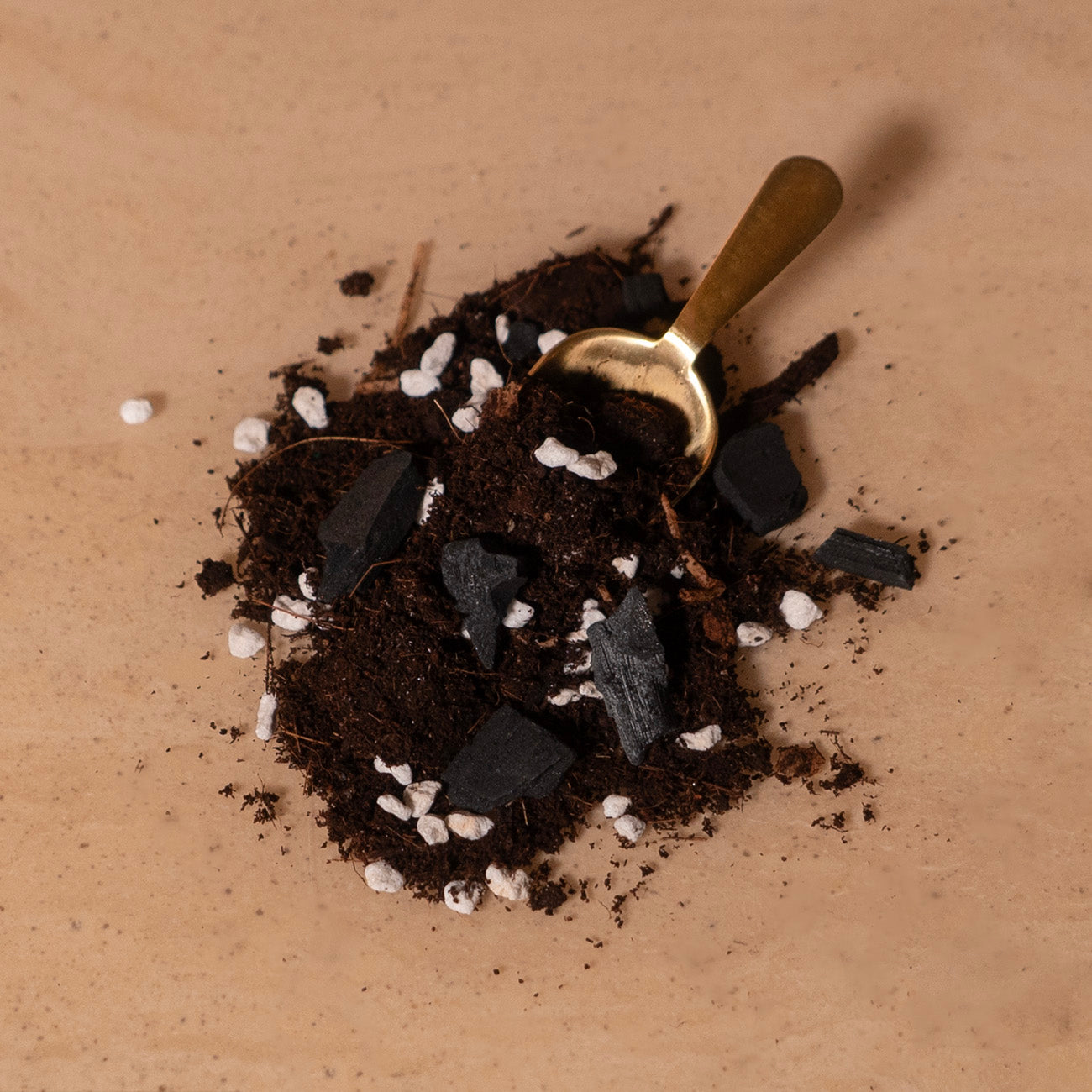 A spoonful of Aroid mix, consisting of coco coir, perlite, charcoal, bark, and worm castings, resting on a surface with more mix spilled around it.