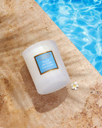 Collines De Provence Scented Candle with a blue label on a stone surface near a pool