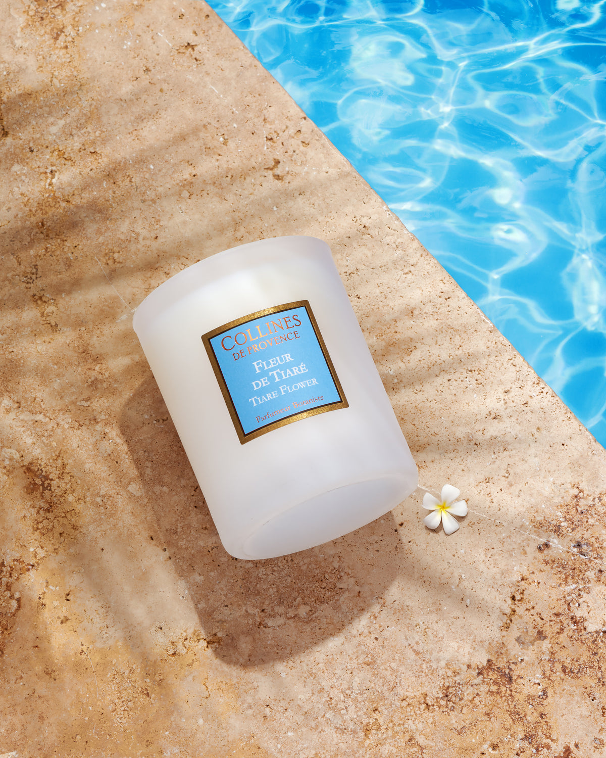 Collines De Provence Scented Candle with a blue label on a stone surface near a pool