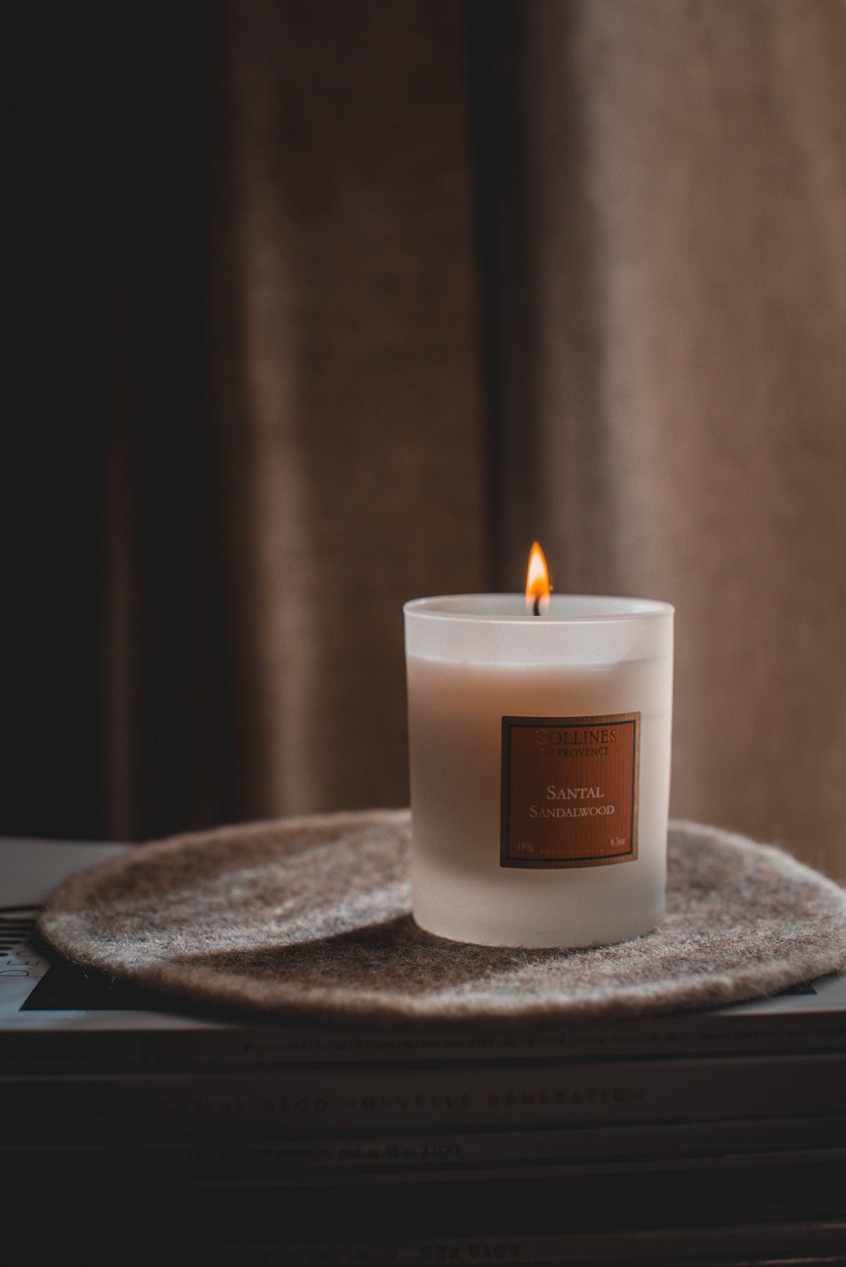 Collines de Provence Sandalwood Scented Candle with a label on a textured surface with a blurred background
