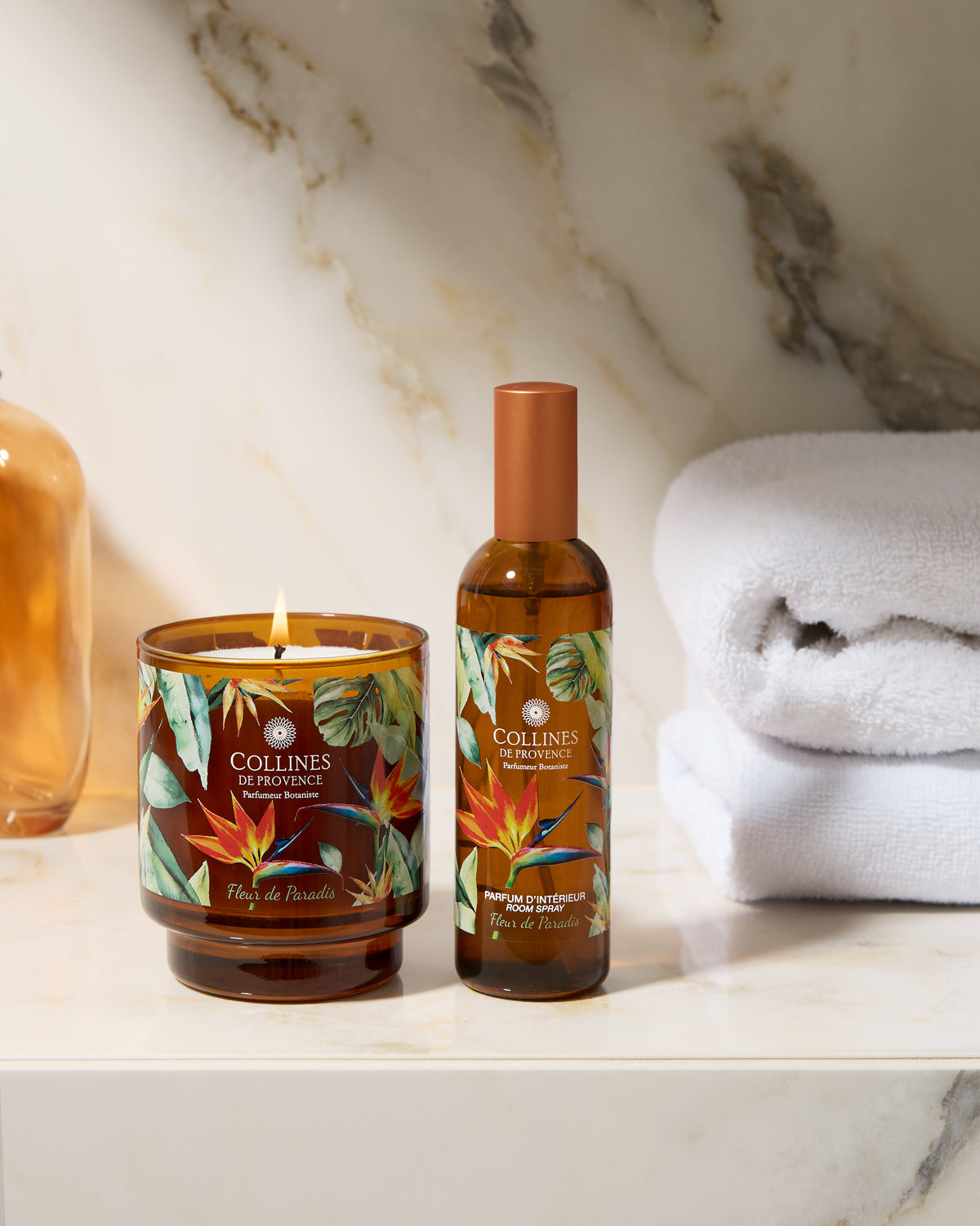 Collines de Provence scented candle and room spray bottle on a marble surface with towels in the background