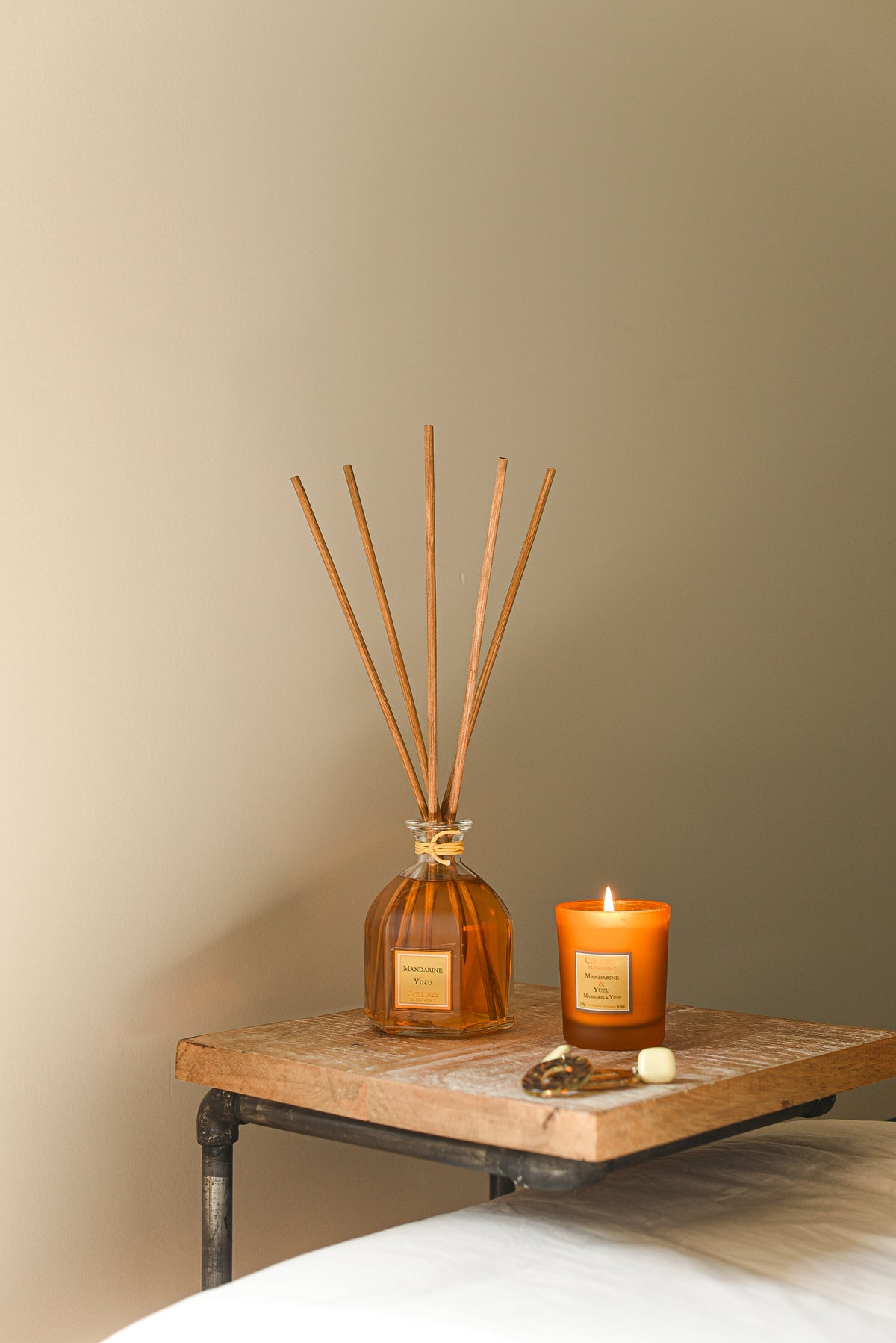 A scented candle and a reed diffuser with Mandarin & Yuzu fragrance, placed on a wooden table.