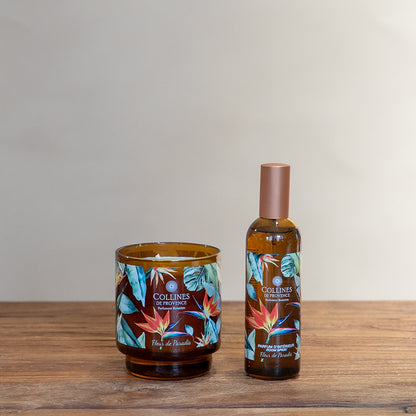 Collines de Provence Paradise flower scented candle and room spray bottle on a wooden surface with a plain background