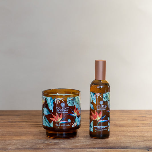 Collines de Provence Paradise flower scented candle and room spray bottle on a wooden surface with a plain background