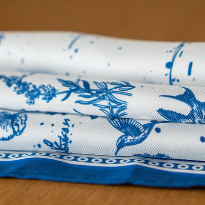 Folded silk scarf with blue floral and butterfly pattern on a wooden surface