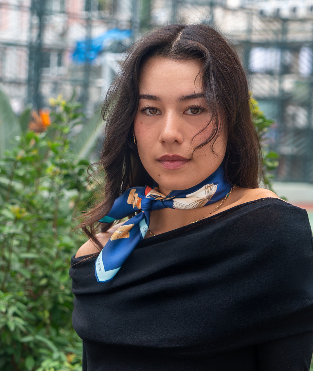 Woman wearing a black top and colorful silk scarf with a blurred outdoor background
