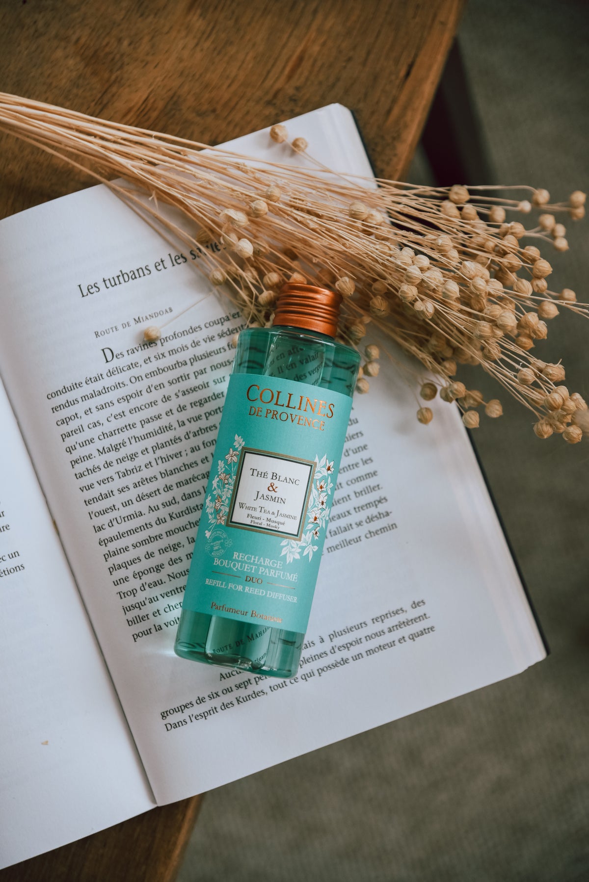 Collines De Provence white tea and jasmine Diffuser refill bottle on an open book with dried herbs