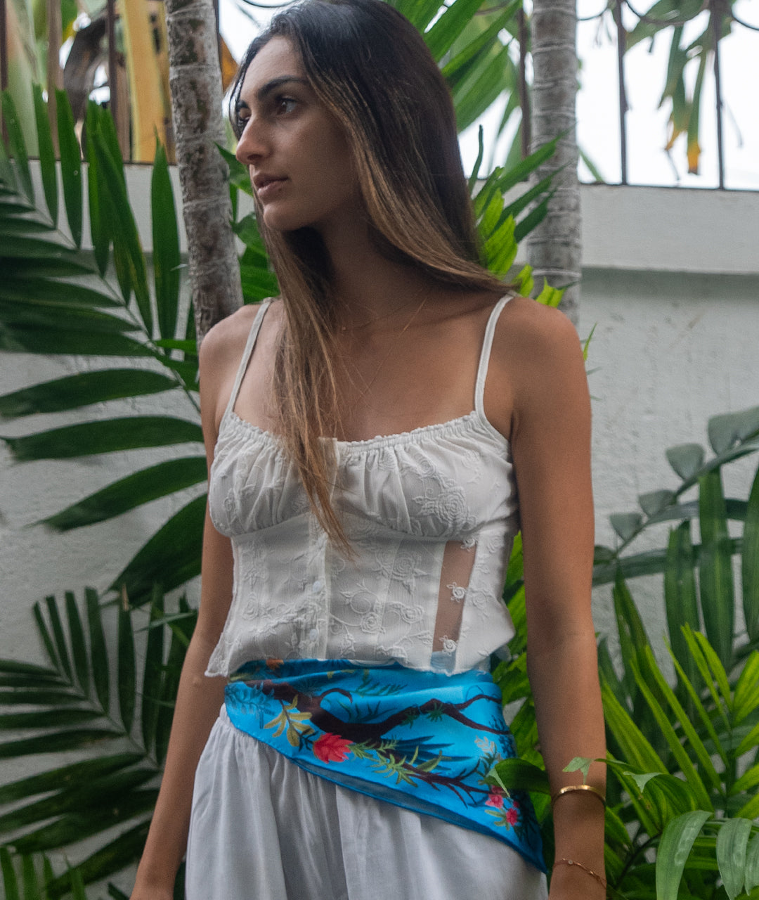 Woman wearing a white top and blue botani bloom silk scarf with floral patterns in a tropical setting