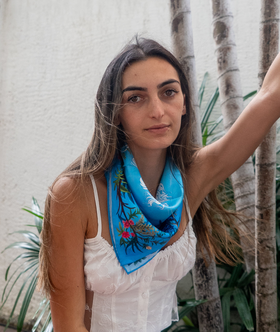 Woman wearing a blue silk scarf with floral patterns in an outdoor setting
