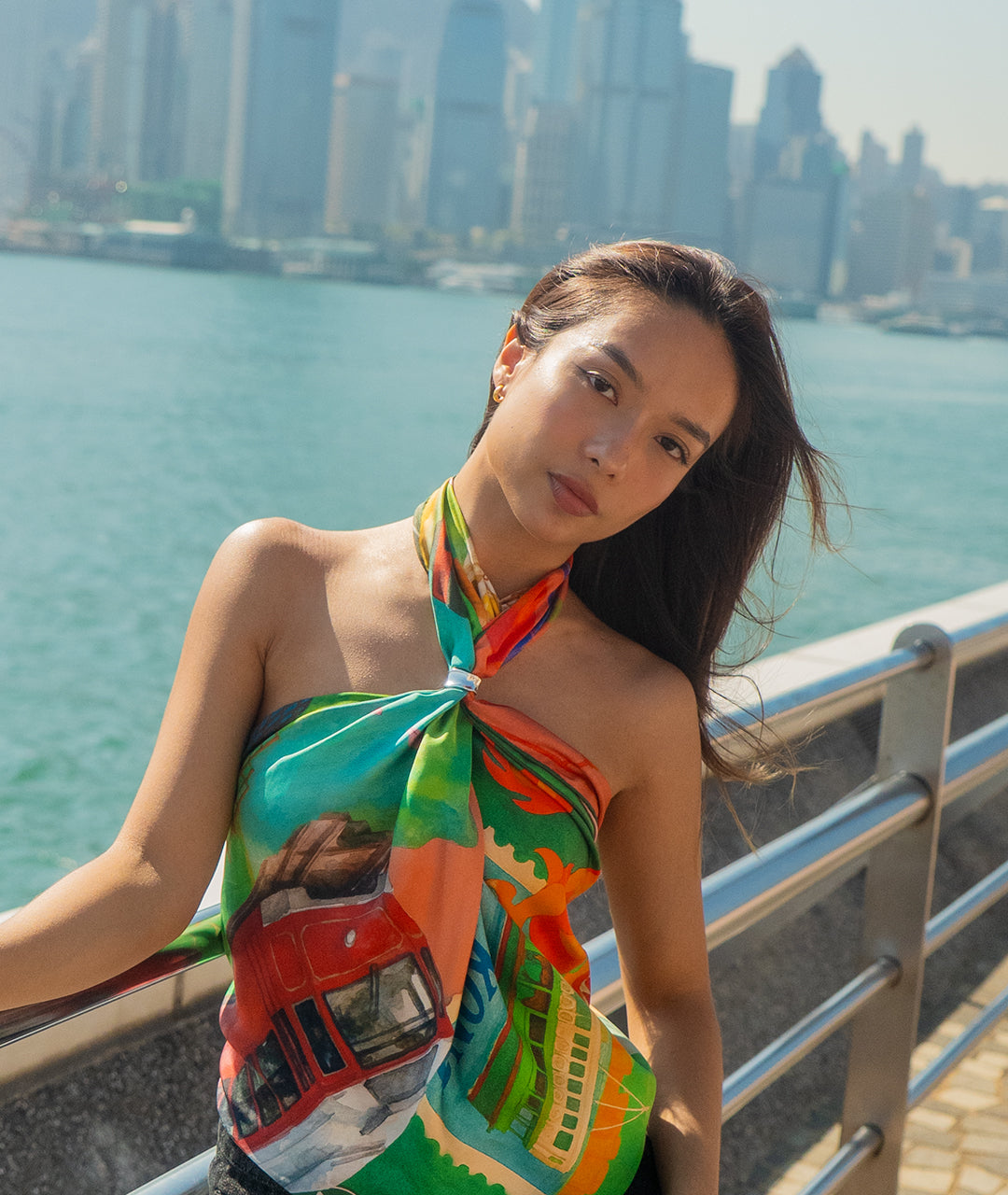 Woman in a colorful Botani Bloom scarf as a top with a cityscape and water in the background