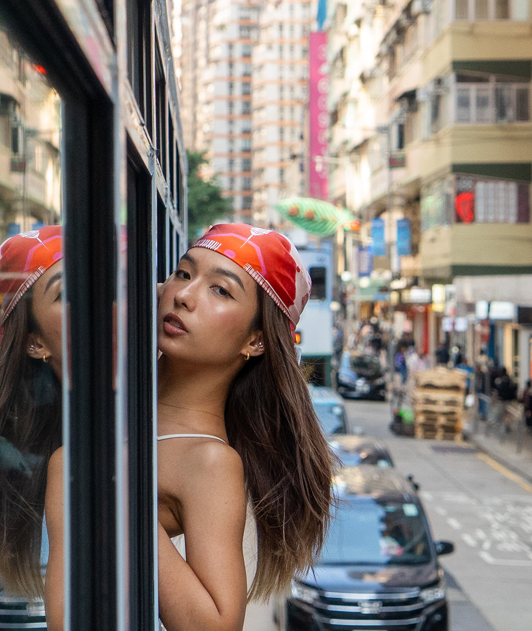 Woman with an orange head scarf looking out of a tram window on a busy street.