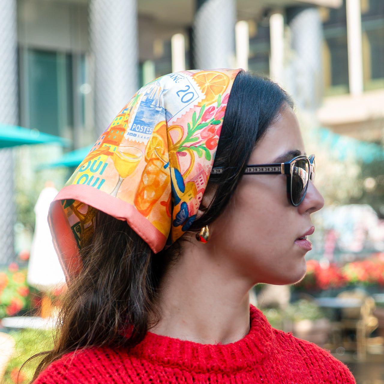 Woman wearing a colorful scarf and sunglasses with a blurred outdoor background