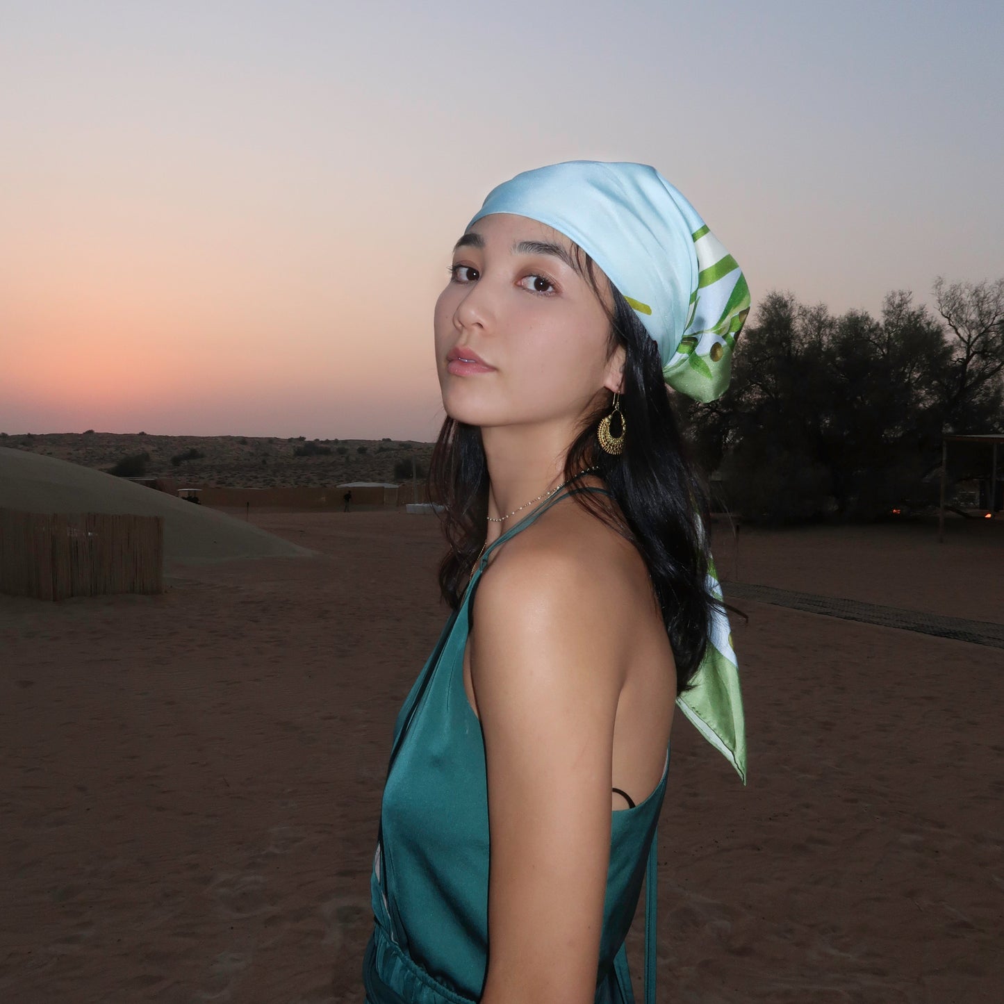 Woman in a green dress and blue and green botani bloom headscarf standing in a desert at dusk.