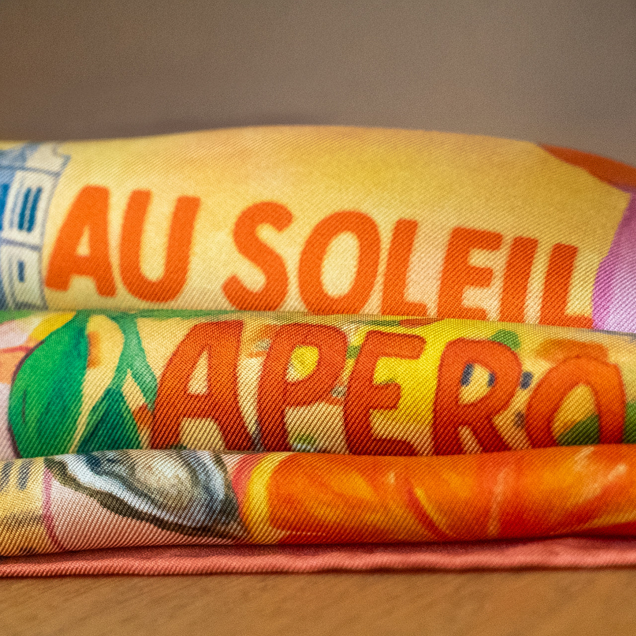 Colorful scarf with text 'AU SOLEIL APERO' on a wooden surface
