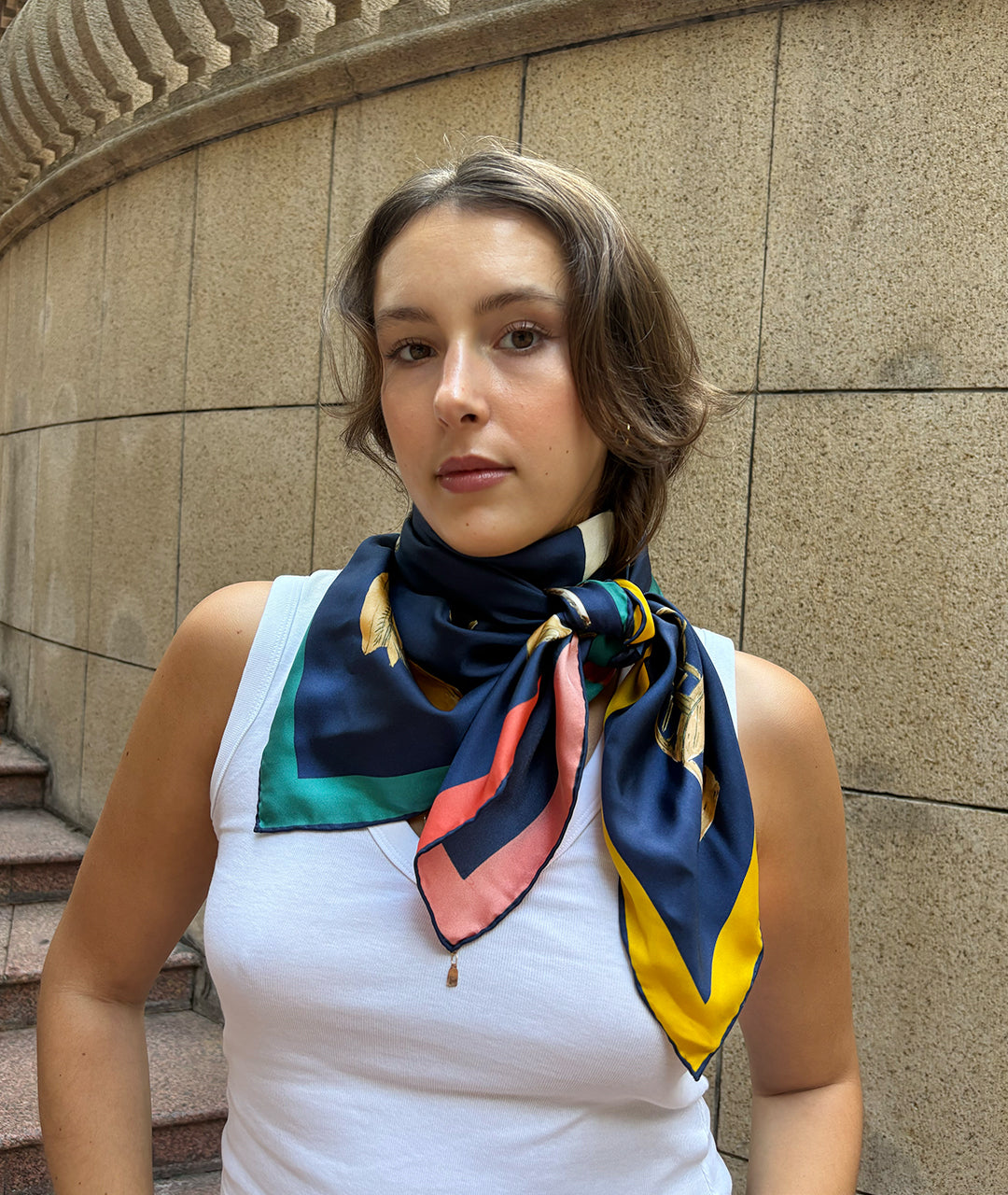 Woman wearing a colorful botani bloom silk scarf around her neck against a stone wall background