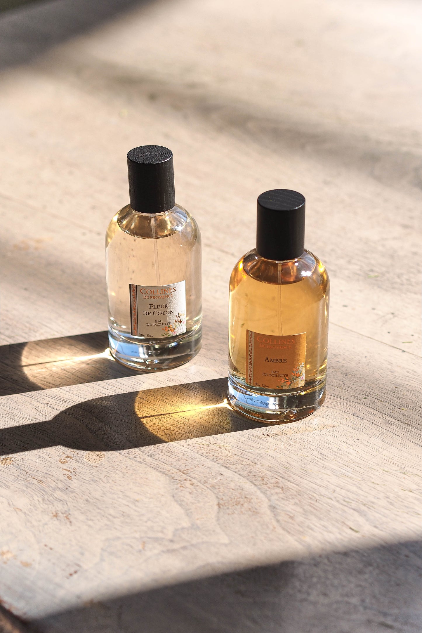 Amber perfume and Coton perfume bottles on a marble surface with sunlight casting shadows.