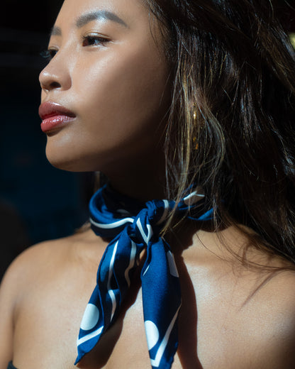 Woman wearing a blue and white patterned scarf around her neck with a blurred background