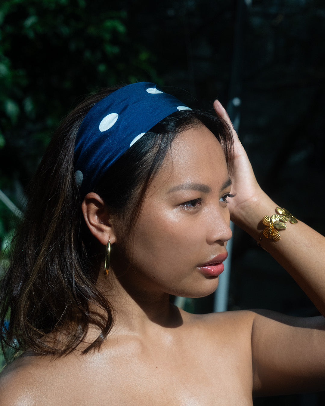 Woman wearing a botani bloom scarf as a headband with white polka dots, posing outdoors.