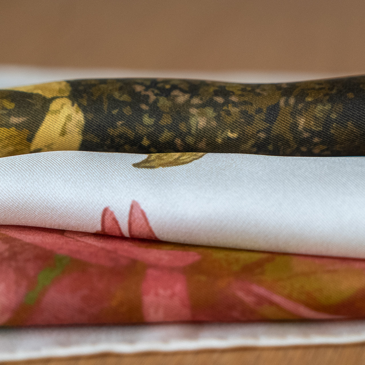 Stack of floral-patterned silk scarves on a wooden surface