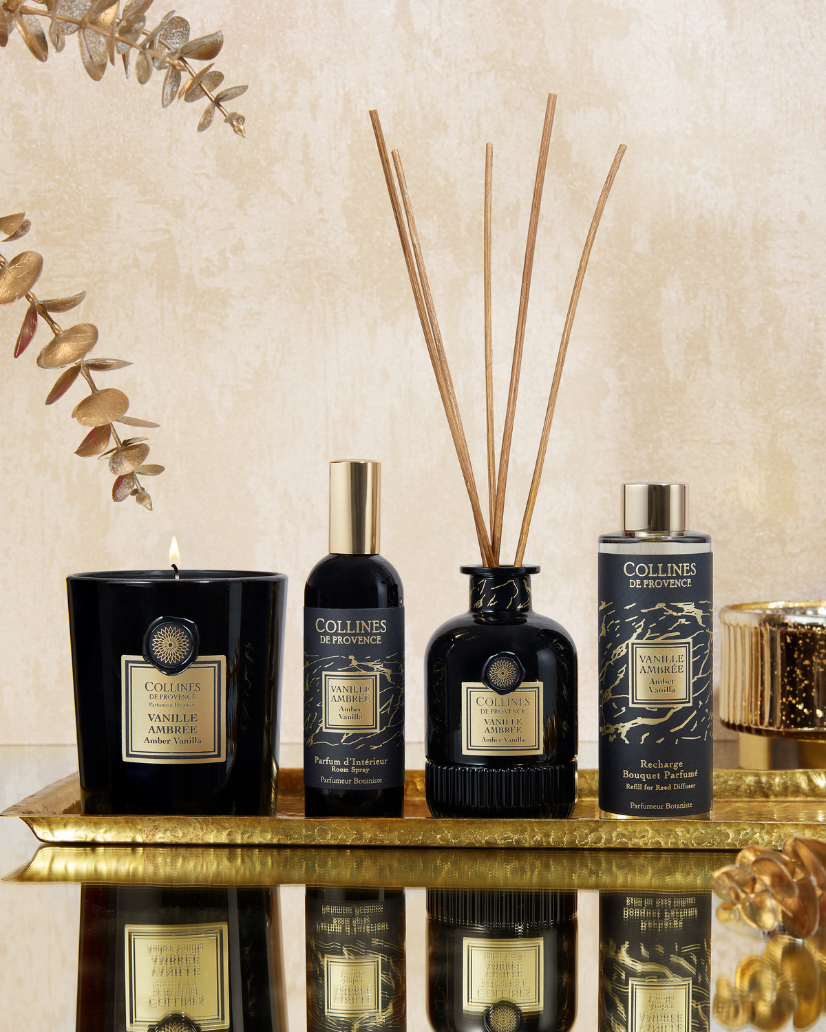 Collines de Provence vanilla amber collection fragrance products including a candle, diffuser, diffuser refills, and room spray on a reflective surface.