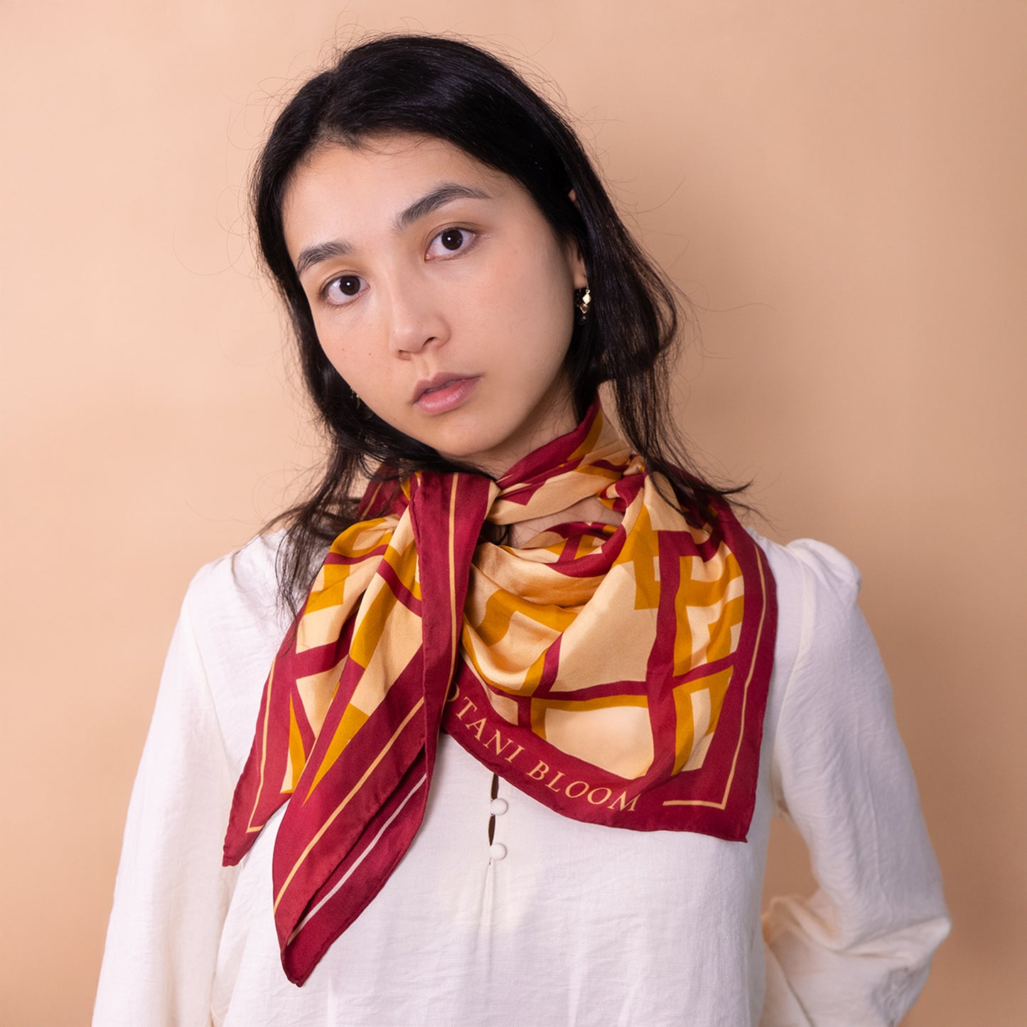 Woman wearing a patterned scarf with 'Botani Bloom' branding against a beige background