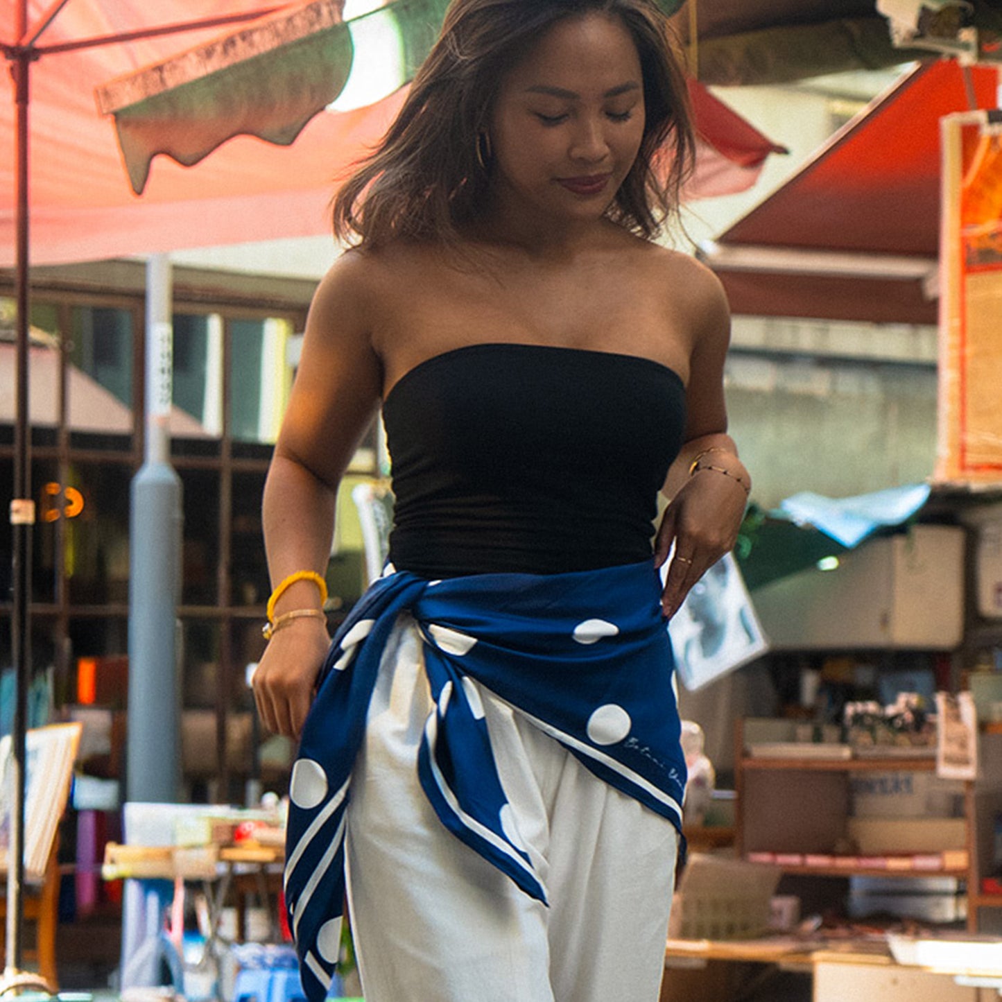Woman wearing a black strapless top and blue and white patterned scarf in an outdoor setting.