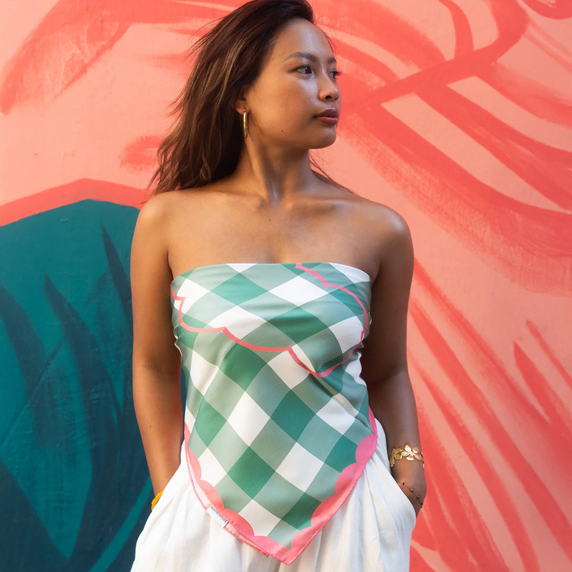 Woman wearing a green and white checkered scarf as a top against a colorful abstract background