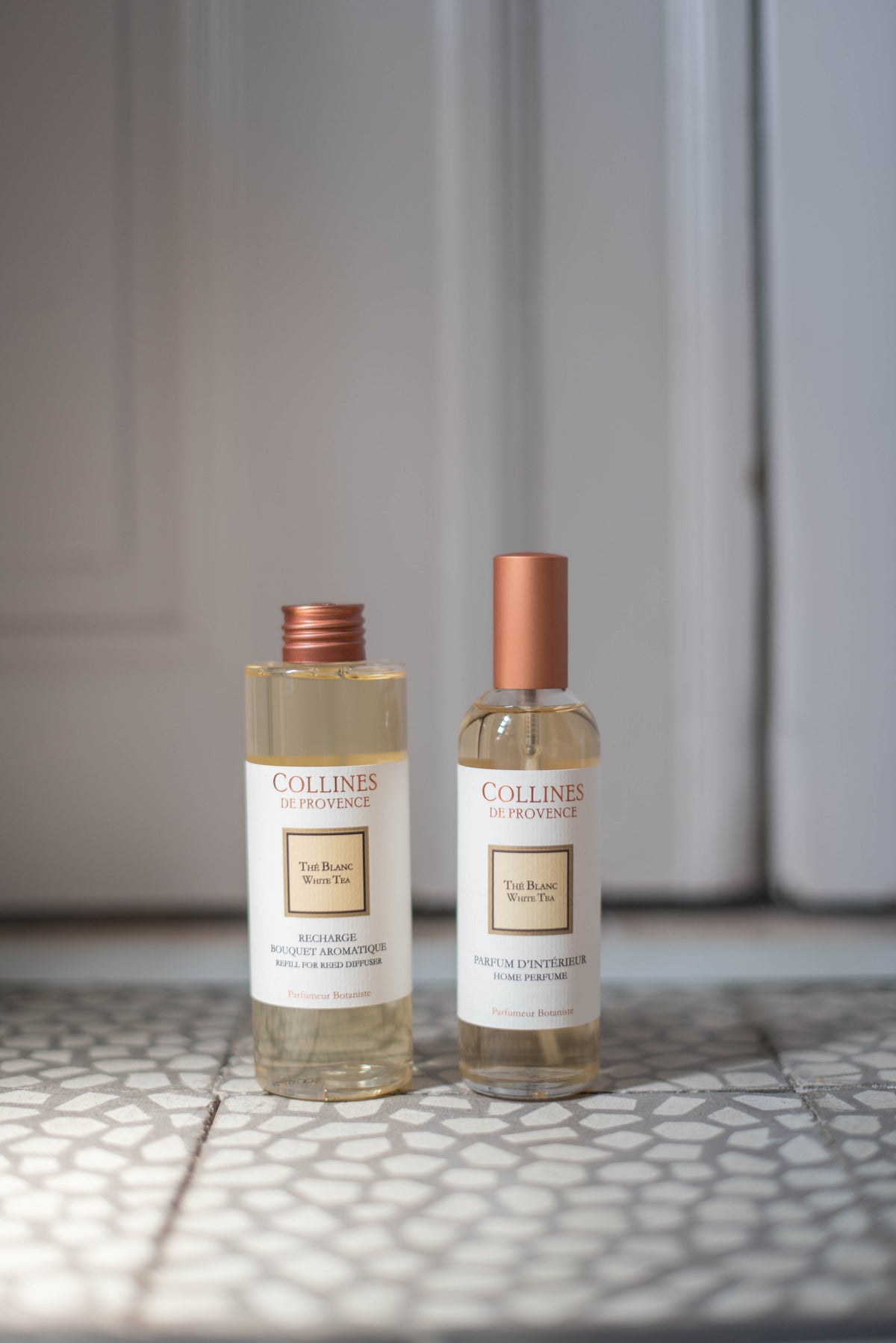 Two bottles of Collines De Provence white tea Diffuser refill and Room spray on a textured surface with a neutral background