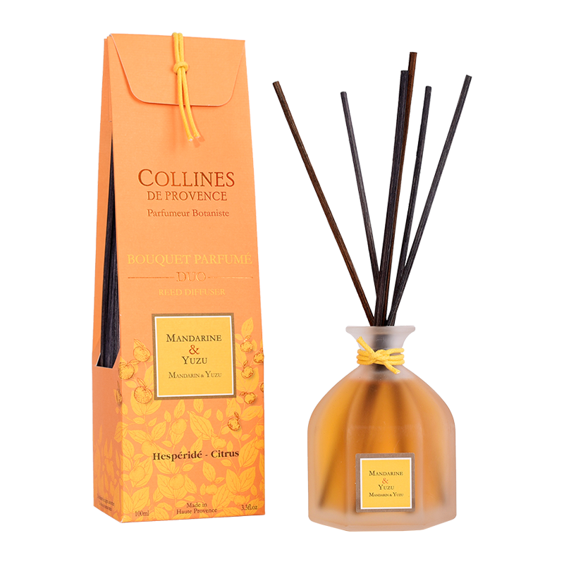 A Mandarin & Yuzu reed diffuser by Collins de Provence in a clear glass bottle with black reeds, next to its orange packaging box.
