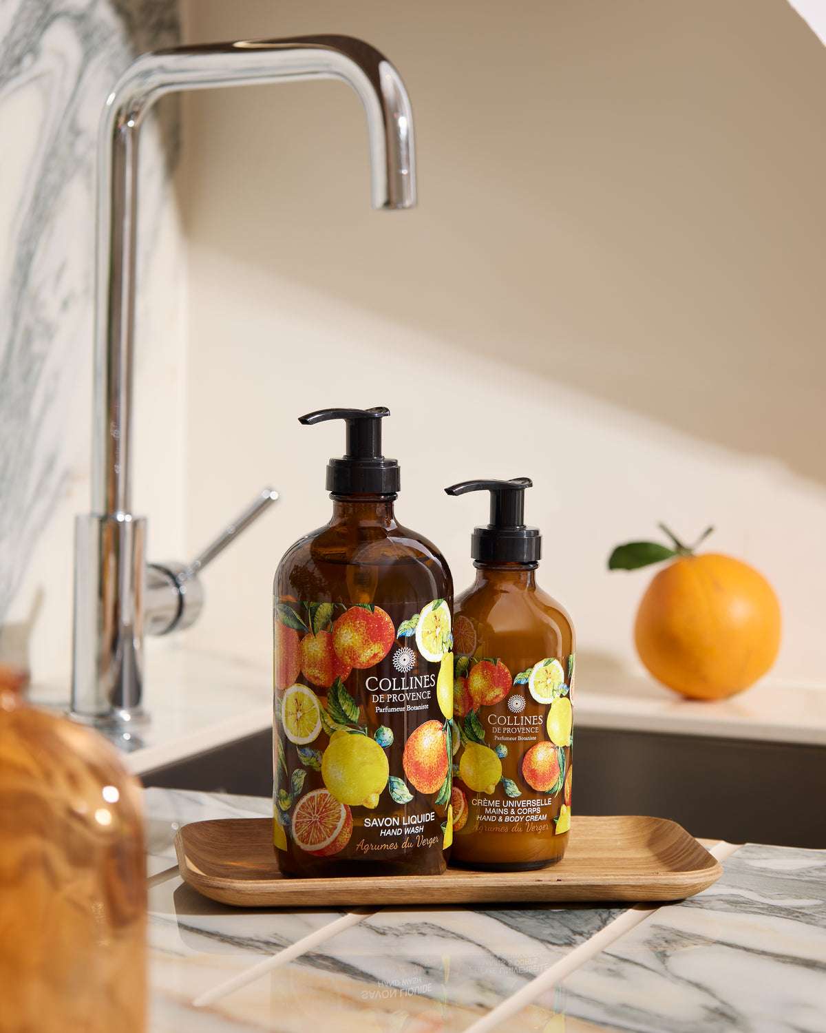Collines De Provence Liquid soap and Body lotion, with a faucet and orange fruit on the background
