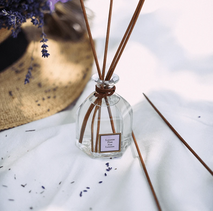 Collines de provence Fine lavender reed diffuser bottle with reeds on a white surface with lavender flowers.
